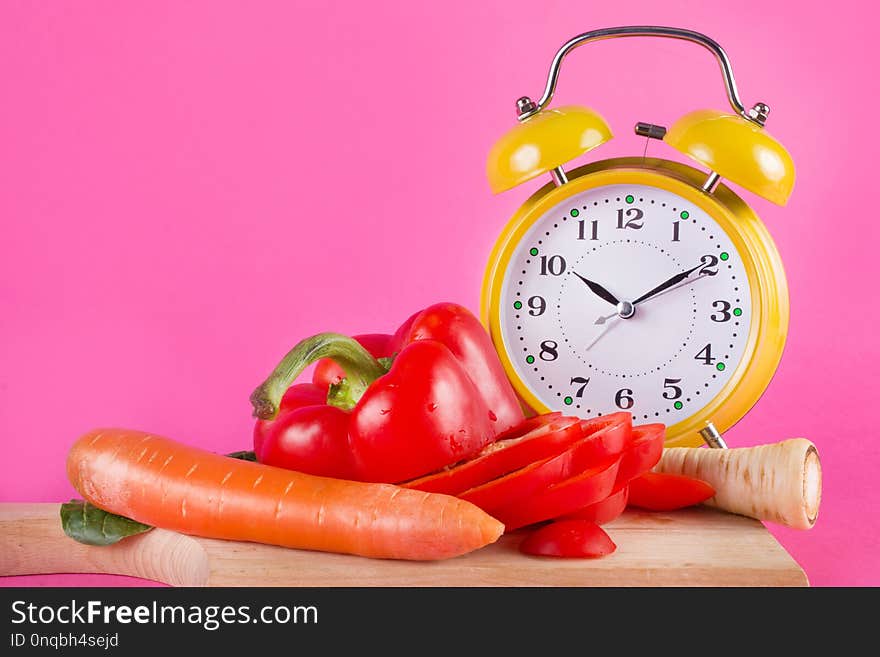 Fresh vegetables on a wooden kitchen board and retro clock isolated on pink