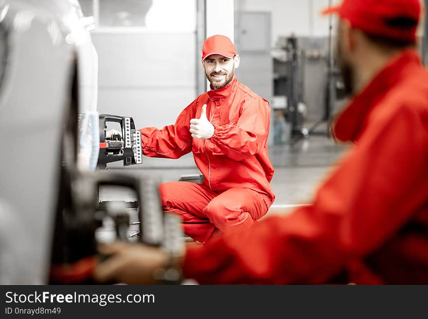 Two auto mechanics in red uniform fixing disk for wheel alignment on a luxury car at the car service. Two auto mechanics in red uniform fixing disk for wheel alignment on a luxury car at the car service