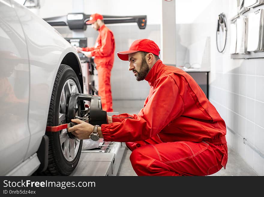 Handsome auto mechanic in red uniform fixing disk for wheel alignment at the car service. Handsome auto mechanic in red uniform fixing disk for wheel alignment at the car service