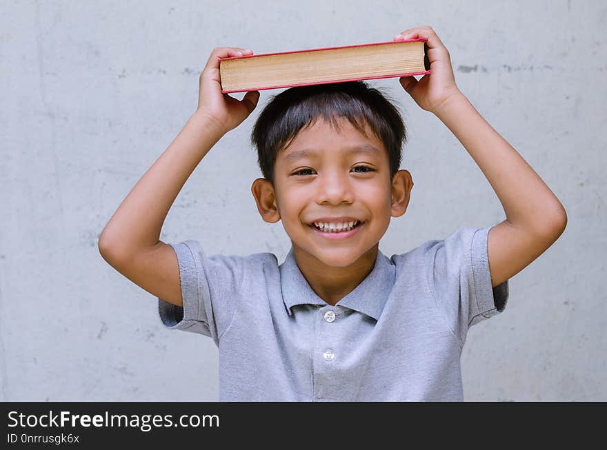 Asian child feeling happy and smiling with a book and put a book on his head. Asian child feeling happy and smiling with a book and put a book on his head.