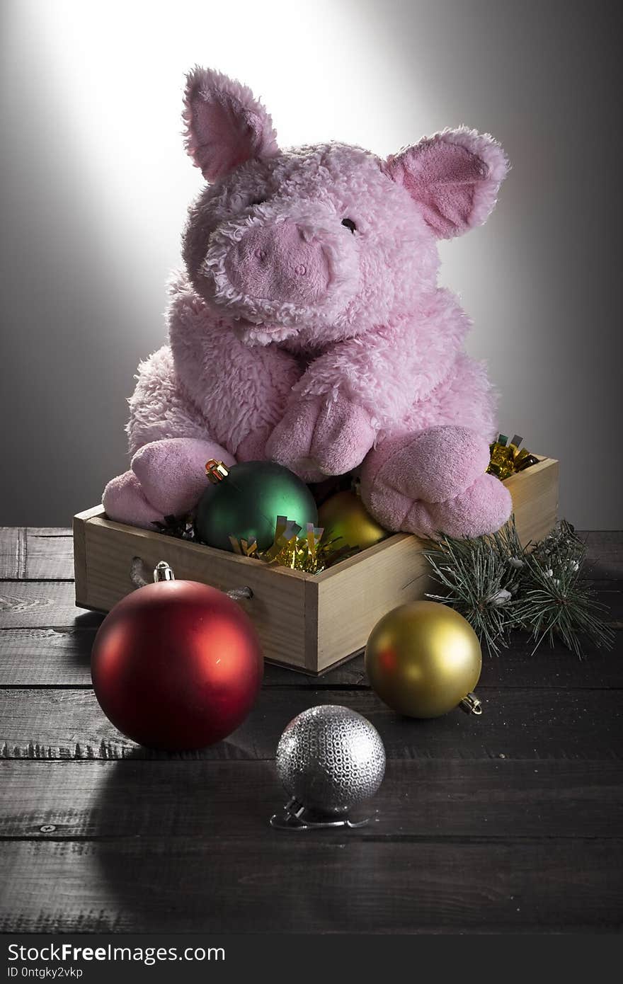 Toy pig sitting on box with New year balls on wooden surface. Festive card, Chinese New Year of Pig, Zodiac symbol 2019