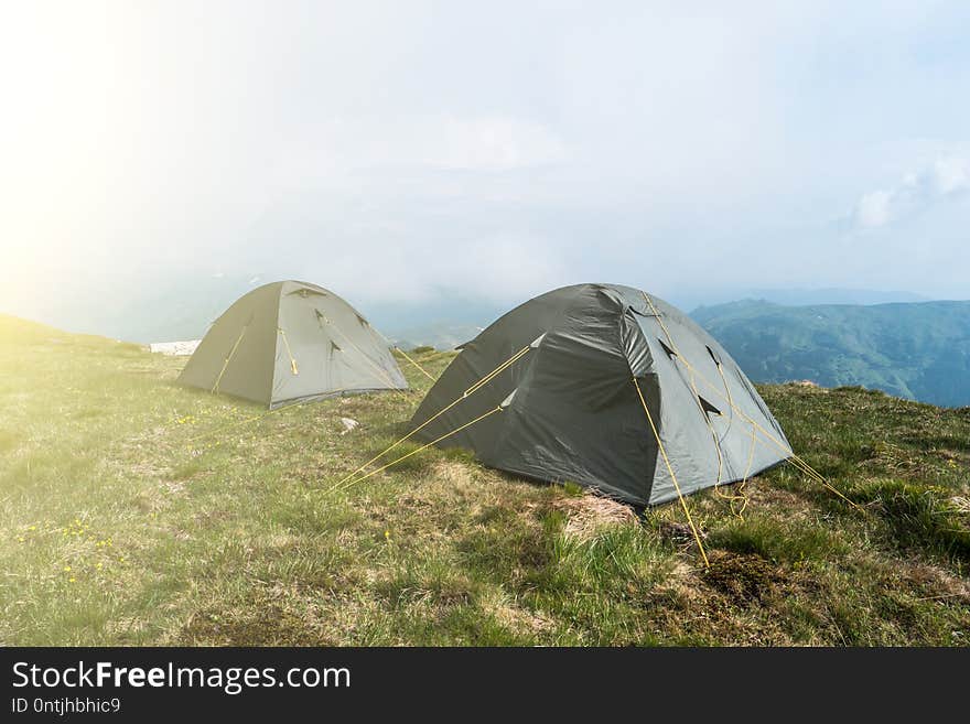 Tourist tents in camp among meadow in the mountain. Camping outdoor, tents in mountains. Tourist tents in camp among meadow in the mountain. Camping outdoor, tents in mountains