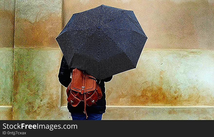 Beautiful girl with a brown leather backpack holding umbrella in the street on a rainy day - visiting Copenaghen