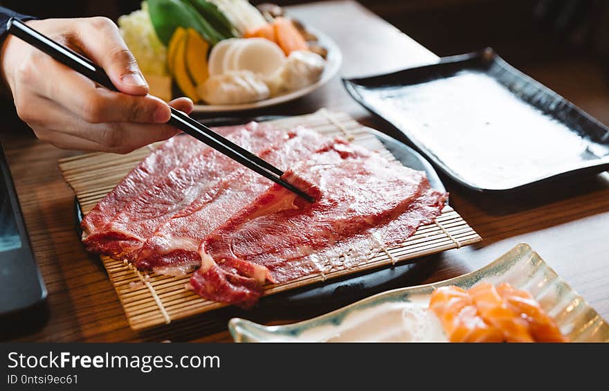 Man holding rare slice Wagyu A5 beef by chopsticks for boiling in Shabu hot pot.