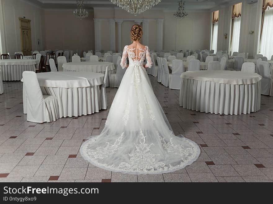 Beautiful bride in a wedding dress in a luxurious white room with a large chandelier. Bride before ceremony. Morning bride.