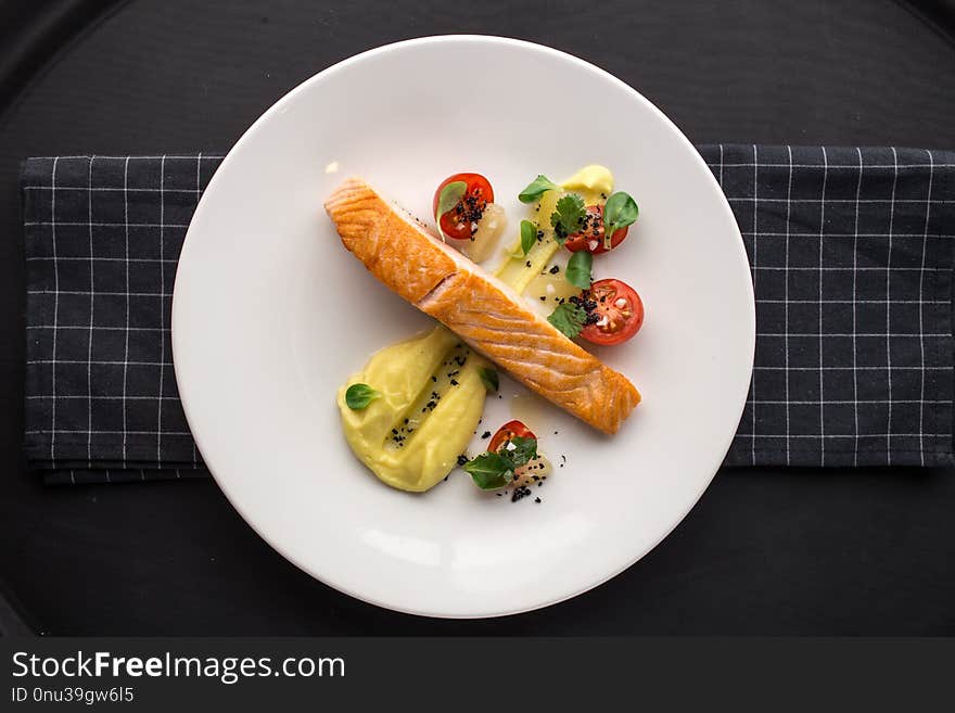 Grilled salmon fillets with potato mash and tomatoes on stone board on black background top view