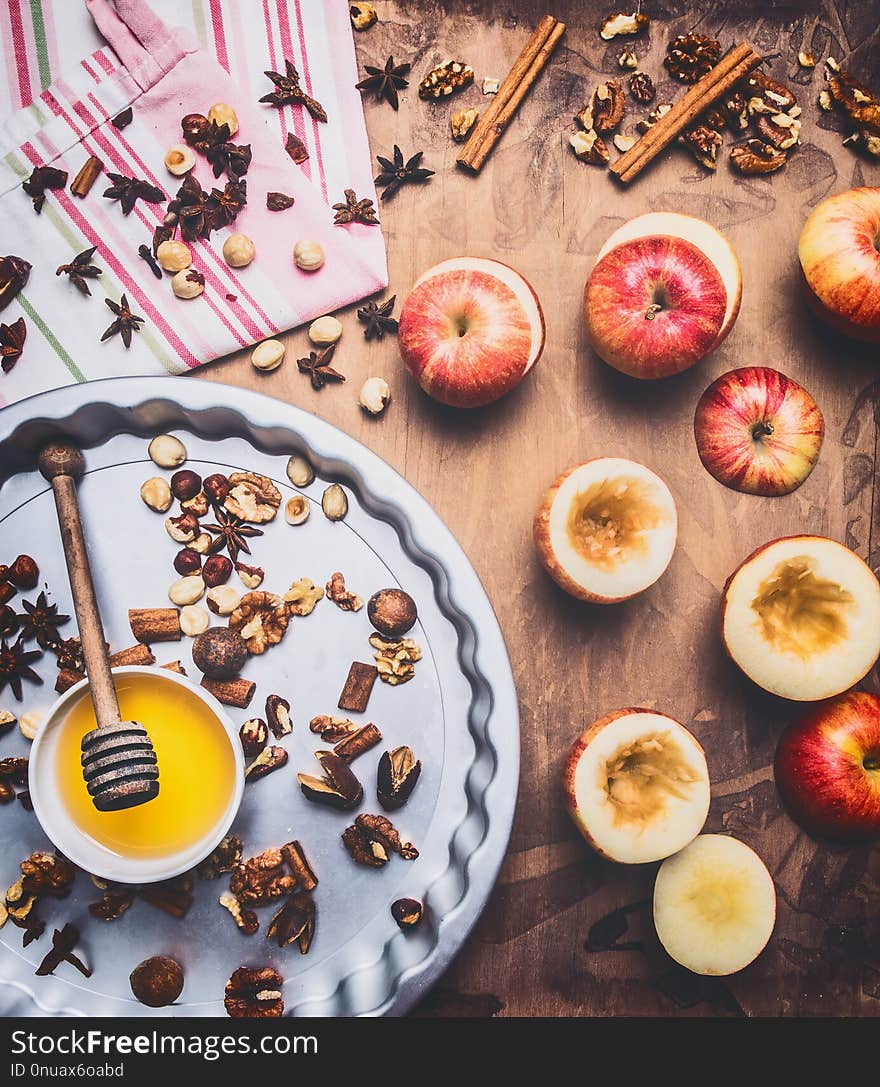 Baked apples with nuts and honey on a round baking sheet on a wooden background, around are lined with ingredients, nuts and