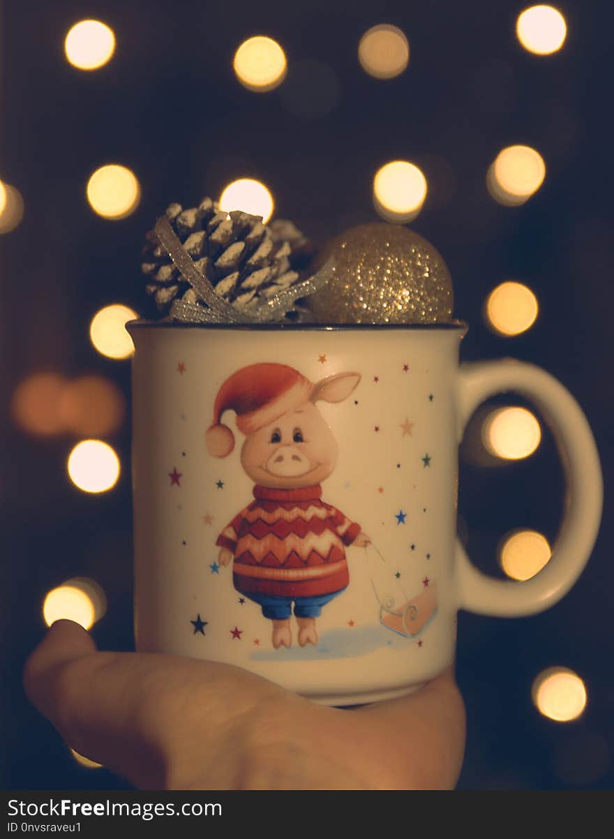 Christmas theme. in the hand of a mug with a pig and Christmas balls. bokeh in the background. Twinkling lights on the holiday