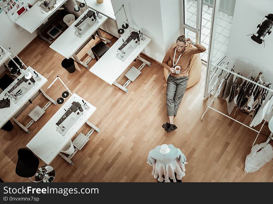 Relaxation. Tall young fashion designer wearing eyeglasses feeling relaxed in a workshop. Relaxation. Tall young fashion designer wearing eyeglasses feeling relaxed in a workshop