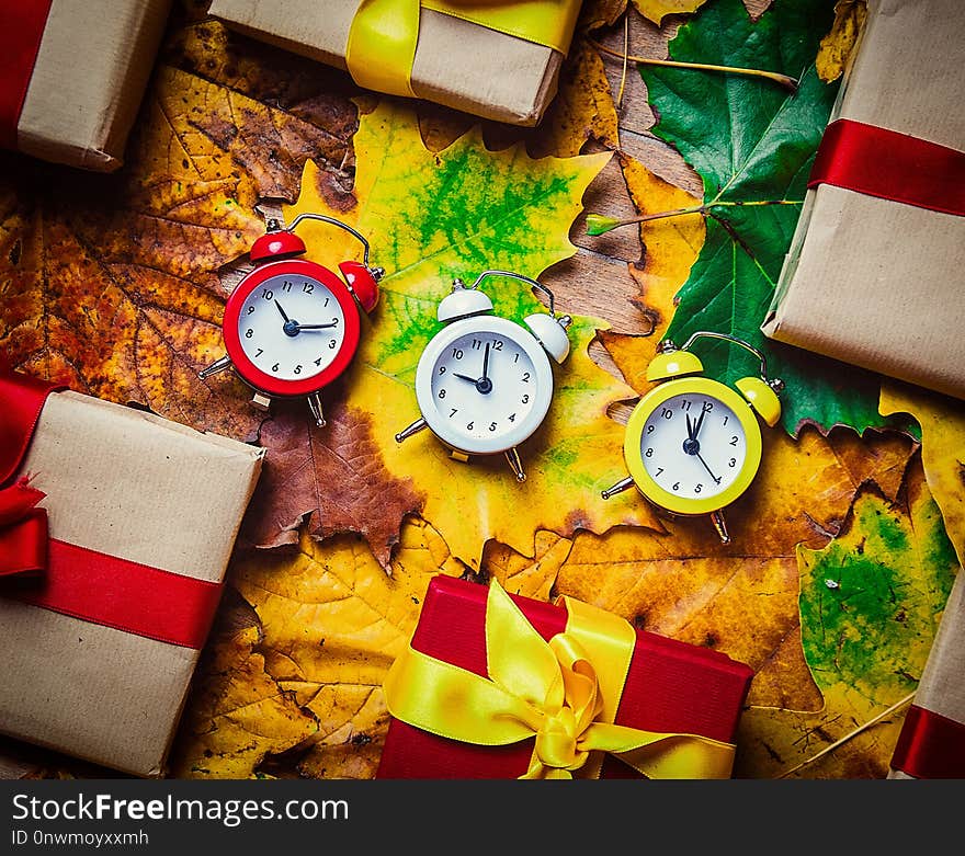 Vintage alarm clocks and maple leaves with Holiday gifts on wooden background