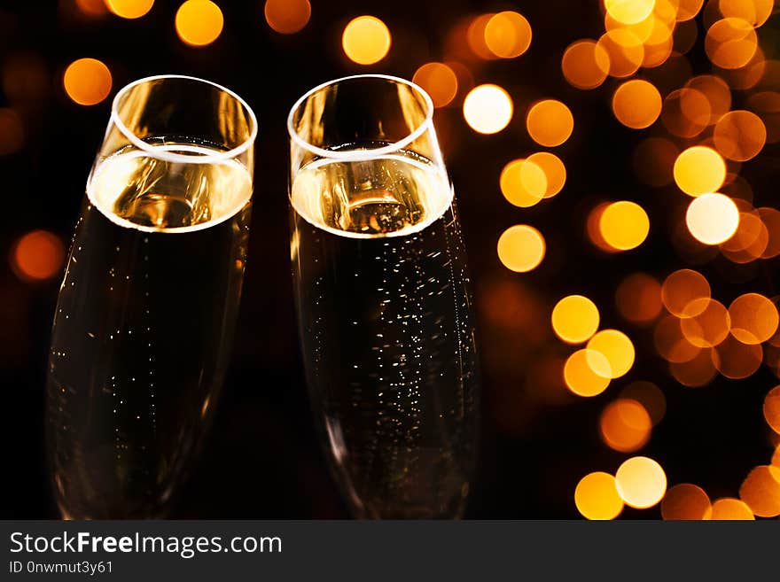 Two glasses of champagne on black stylish background with golden bokeh circles. Place for text. Festive concept. Two glasses of champagne on black stylish background with golden bokeh circles. Place for text. Festive concept.