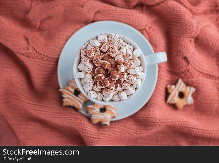 Coffee cup with marshmallow and stars cookies on warm knitted coral blanket. Cozy and moody concept. Top view