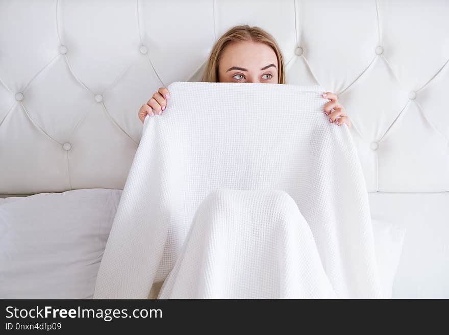 Pretty young woman with white hair hiding face behind blanket in the morning bedroom, comic girl