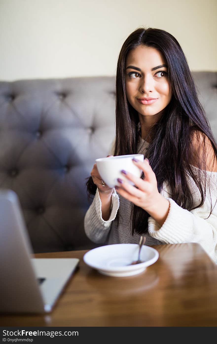 Young beautiful woman drinking coffee at cafe bar while use laptop