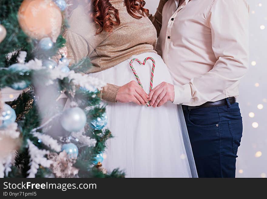 Couple makes heart with candy canes on background of a pregnant belly. Cropped. Christmas mood