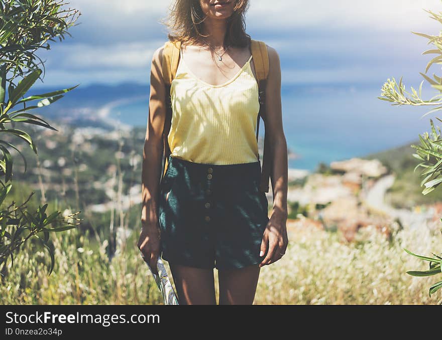 Hipster young girl with bright backpack looking at a map and poining hand the travel plan. View from the back of the tourist traveler on background mountain, sea. Mock up for text message