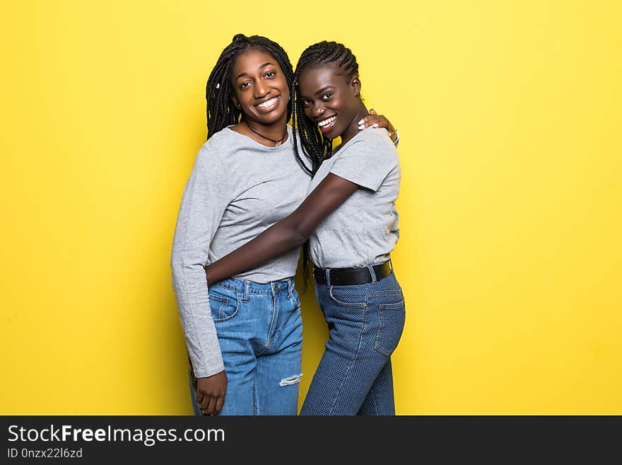 Photo of lovely african womens stand closely hug each other embrace isolated over yellow background. People and diversity concept. Photo of lovely african womens stand closely hug each other embrace isolated over yellow background. People and diversity concept