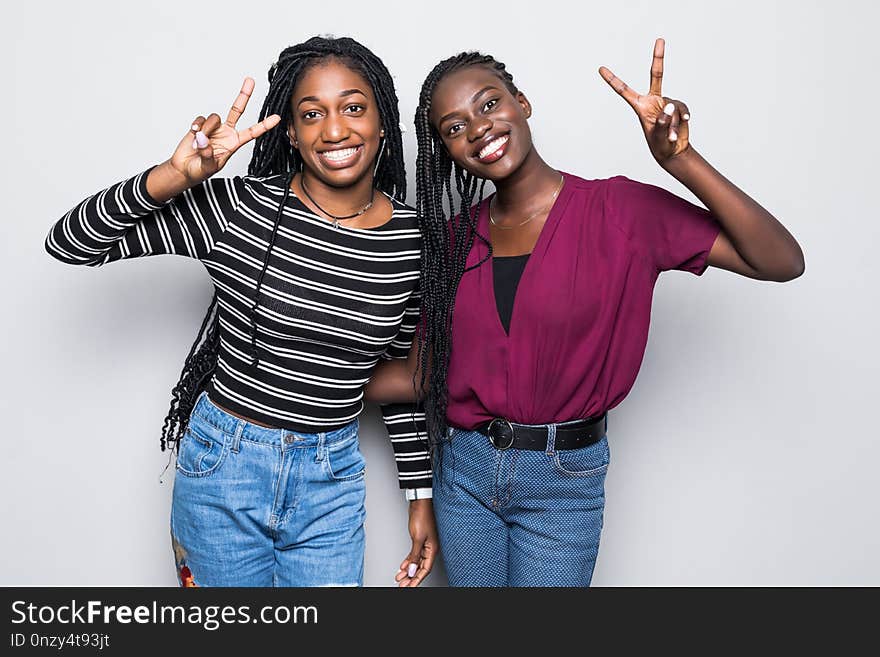 Portrait of a two african girlfriends showing two fingers sign on gray background