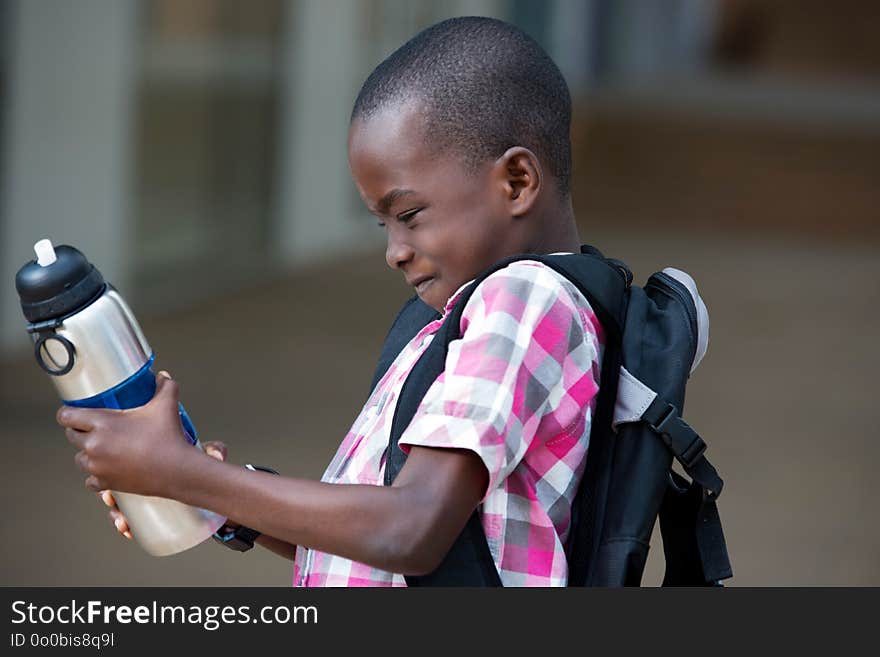 Schoolboy looking and trying to open his bottle of water that he holds in his hands. Schoolboy looking and trying to open his bottle of water that he holds in his hands