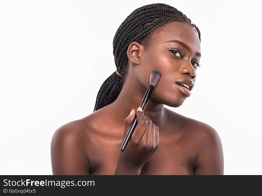 Beauty portrait of a smiling beautiful half naked african woman applying make-up with a brush and looking at camera isolated over