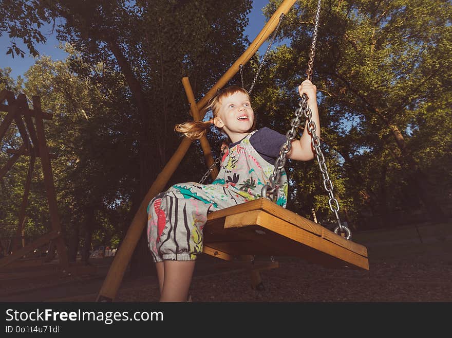 Little girl is having fun on a swing in city park