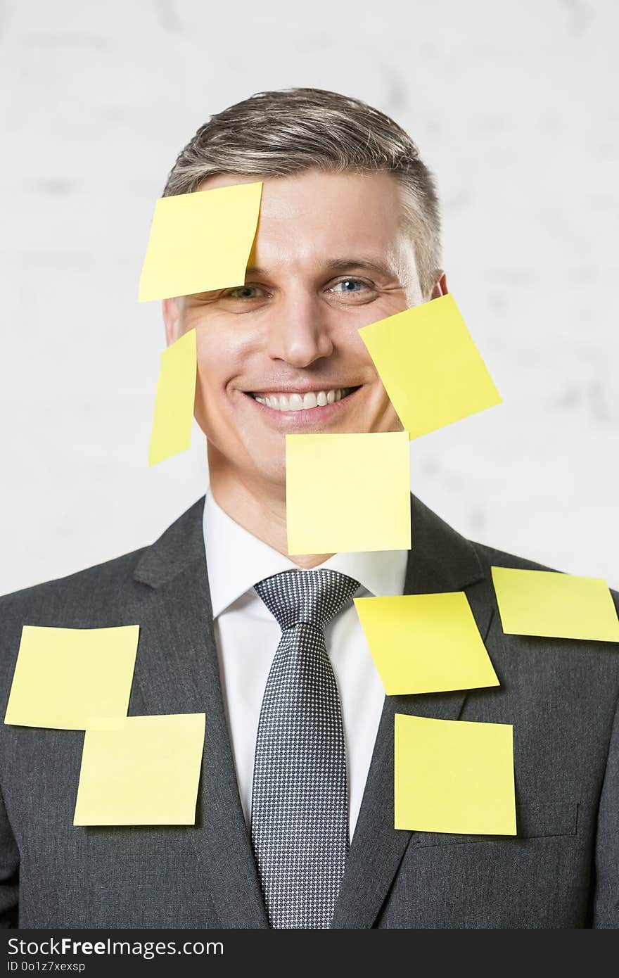 Portrait of smiling mature businessman with blank yellow adhesive notes on face and suit at office