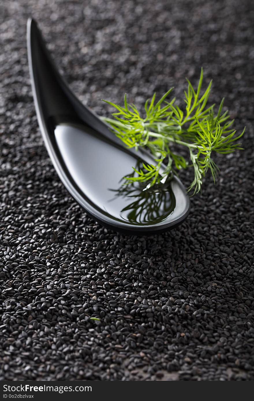 Plant oil in small bowl with dill branches on a background of black sesame. Copy space. Plant oil in small bowl with dill branches on a background of black sesame. Copy space