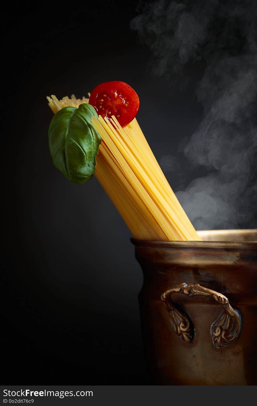 Raw spaghetti with tomato and basil in old brass pan. Black background. Copy space