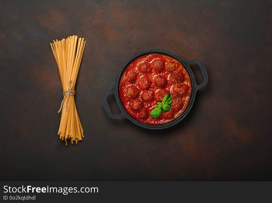 Meatballs in tomato sauce with spices, pasta and basil in a frying pan on rusty brown background