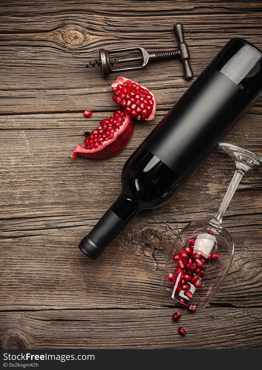 Ripe pomegranate fruit with a glass of wine, a bottle and a corkscrew on a wooden background. Top view with copy space