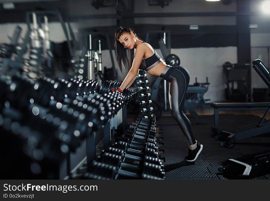 Slim, Bodybuilder Girl, Lifts Heavy Dumbbell Standing In Front Of The Mirror While Training In The Gym. Sports Concept, Fat