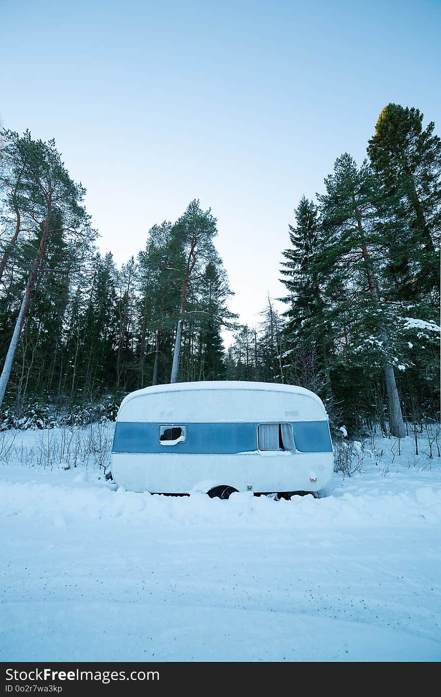 Rundown Camper Trailer in Winter with trees behind it