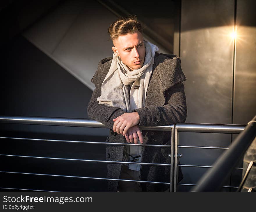 One handsome young man in urban setting in moden city, standing, wearing black coat and scarf in winter day. One handsome young man in urban setting in moden city, standing, wearing black coat and scarf in winter day