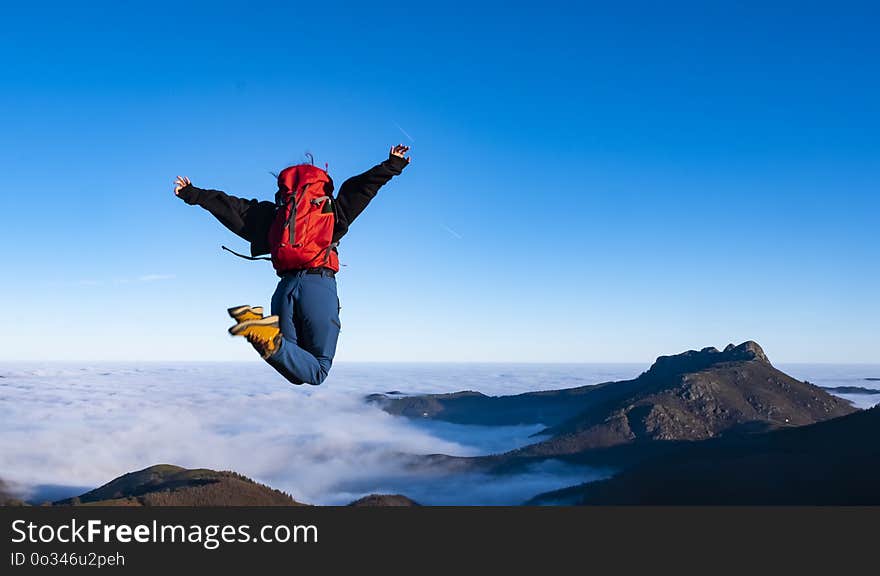 Cheering happy young woman jumping on mountain peak cliff edge