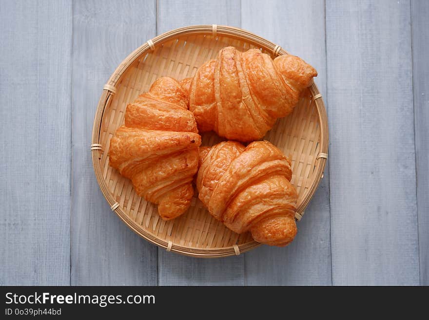 Fresh croissants in a basket weave on the white wood table.