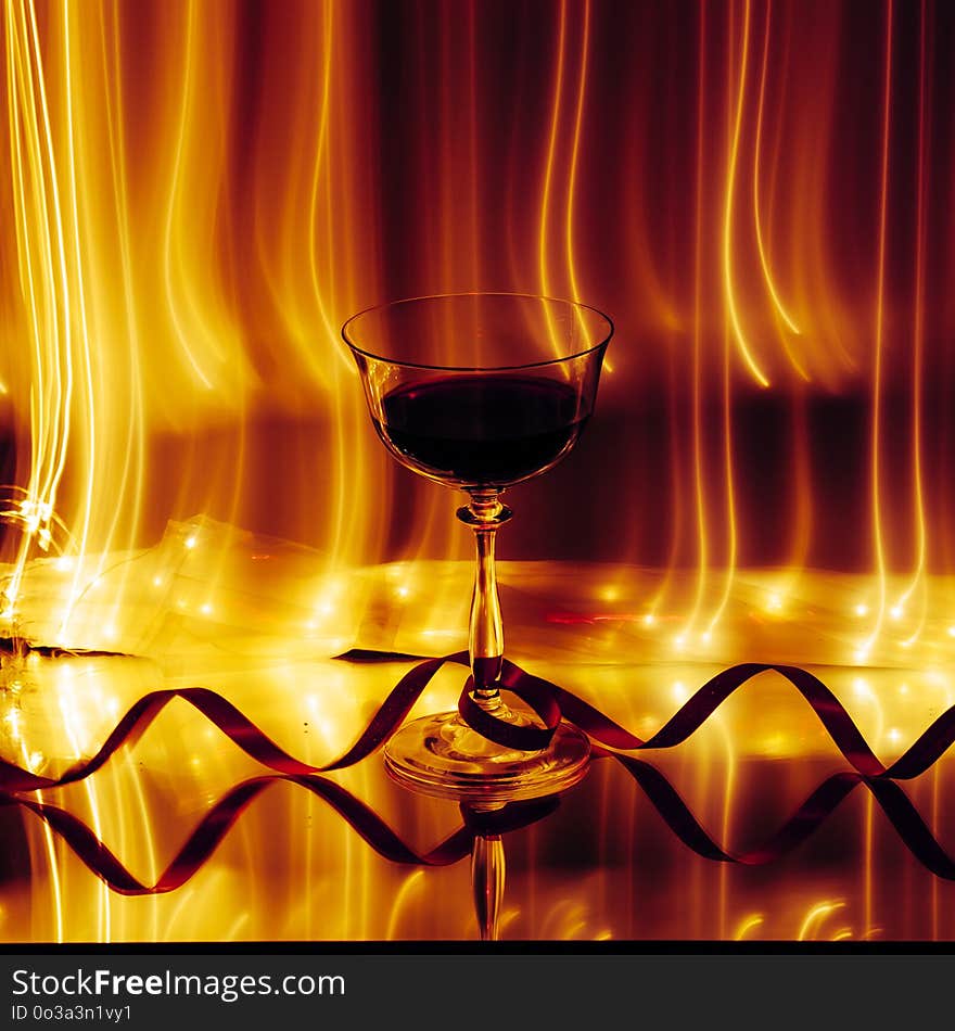 A wine glass, with lines of lights in the background and a red ribbon. Reflection