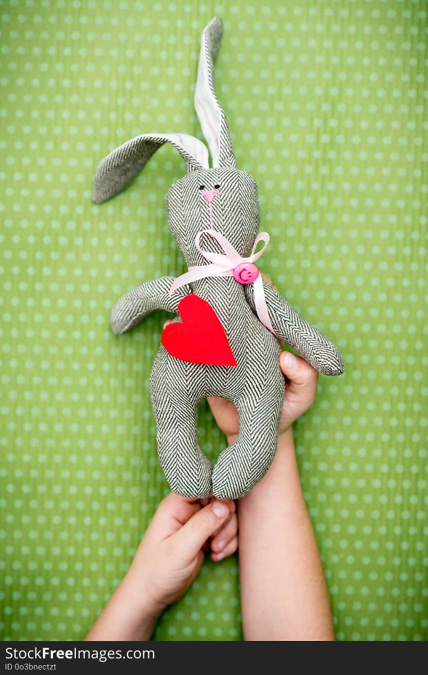 Valentine day. A child holds a rabbit with a red heart in his hand on a green polka dot background. Valentine`s Day. Heart pendant. Space for text. Red heart. Eighth of March. International Women`s Day.