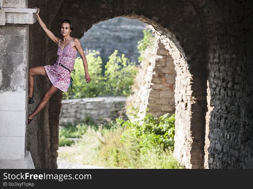 The girl climbs the stone wall. A woman in a summer dress climbs the wall of an old destroyed building. Brick fence. The climber is hanging on the city building. Strengthening the ruined castle