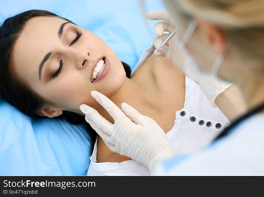 Young female patient visiting dentist office.Beautiful women with healthy straight white teeth sitting at dental chair with open mouth during oral checkup while doctor working at teeth. Dental clinic, stomatology concept. Young female patient visiting dentist office.Beautiful women with healthy straight white teeth sitting at dental chair with open mouth during oral checkup while doctor working at teeth. Dental clinic, stomatology concept