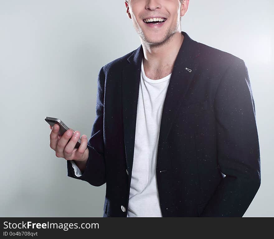 Receiving nice messages. Handsome young man in jacket looking on his smart phone and smiling while standing against grey background. Receiving nice messages. Handsome young man in jacket looking on his smart phone and smiling while standing against grey background