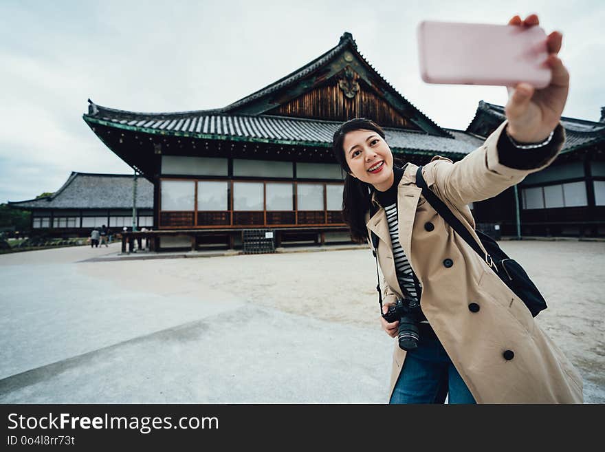 Smiling hipster woman taking selfie photo in nijo jo fitland castle on the background kyoto japan. young girl traveler using smartphone camera app make self portrait. japanese tradition building. Smiling hipster woman taking selfie photo in nijo jo fitland castle on the background kyoto japan. young girl traveler using smartphone camera app make self portrait. japanese tradition building