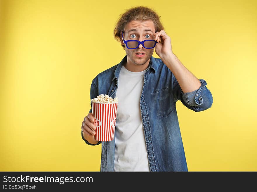 Emotional man with 3D glasses and popcorn during cinema show on color background