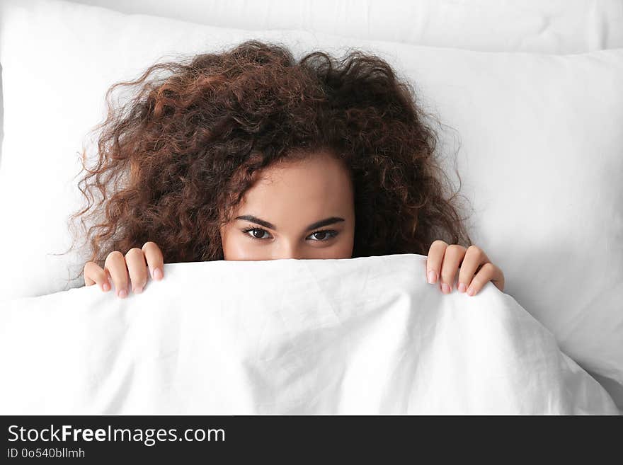 Young African-American woman lying under blanket, top view