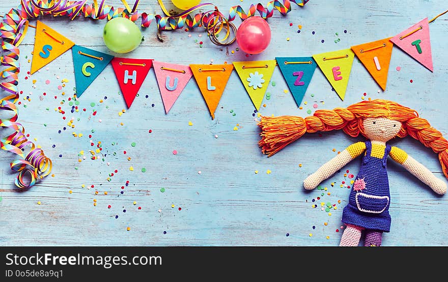 Cute rag doll on a Schul Zeit German background with colorful bunting flags, streamers and confetti over blue wood with copy space for a card or invitation to school children