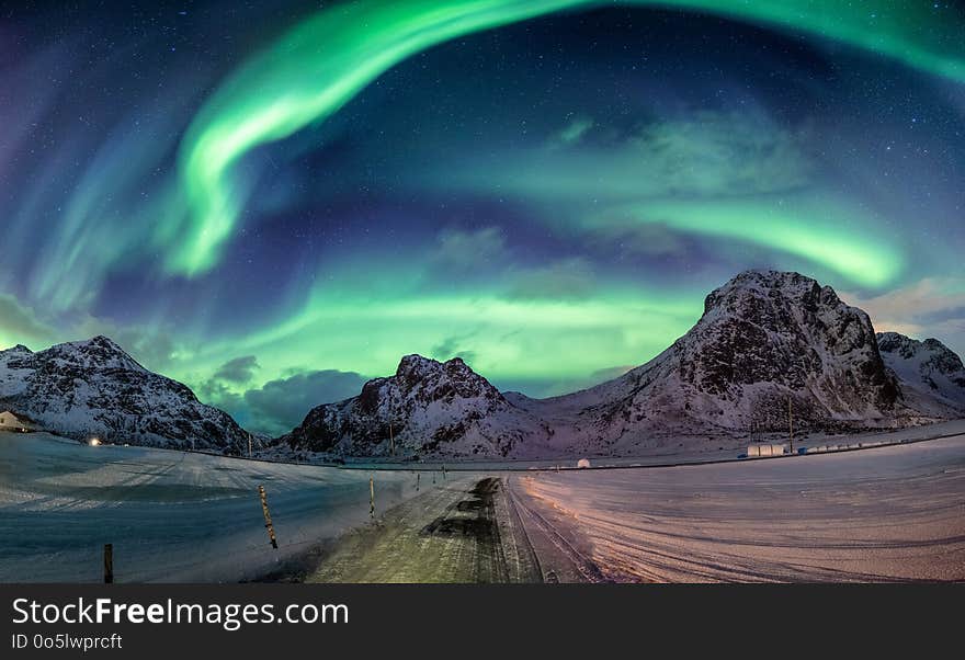 Northern lights explosion on snowy mountain range near coastline at Lofoten islands, Norway