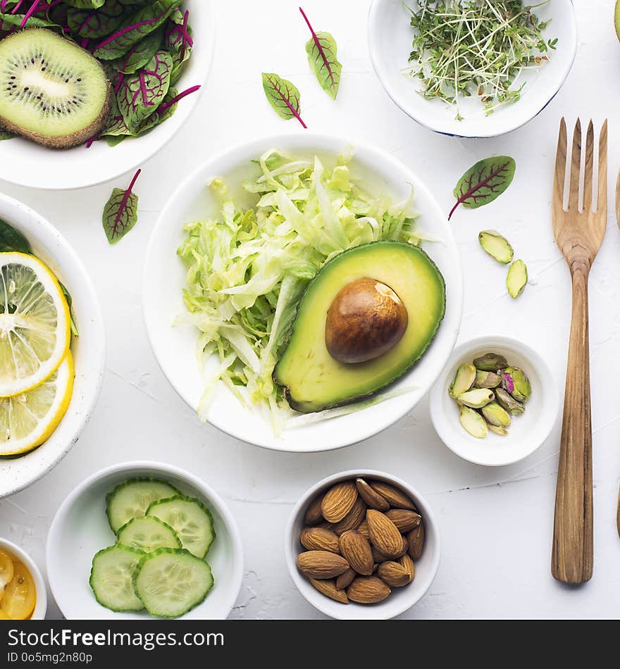 Green ingredients for spring detox salads: spinach, sorrel with red veins, cucumbers, radishes, iceberg lettuce, green peas, avocados, lemon, microgreen, yellow tomatoes on a white background with wooden cutlery. Top view