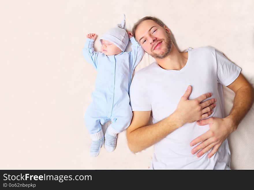 From above shot of handsome men looking at peacefully sleeping baby while lying on soft bed. From above shot of handsome men looking at peacefully sleeping baby while lying on soft bed