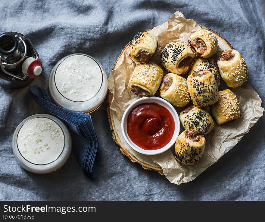 Served appetizers table - minced puff pastry rolls and beer on grey background, top view. Flat lay. Sausage rolls