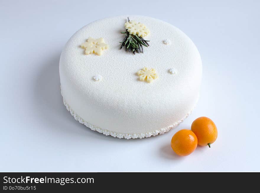 Mousse cake covered with white velvet spray, decorated with chocolate snowflakes, kumquats and fresh rosemary on white background. Mousse cake covered with white velvet spray, decorated with chocolate snowflakes, kumquats and fresh rosemary on white background