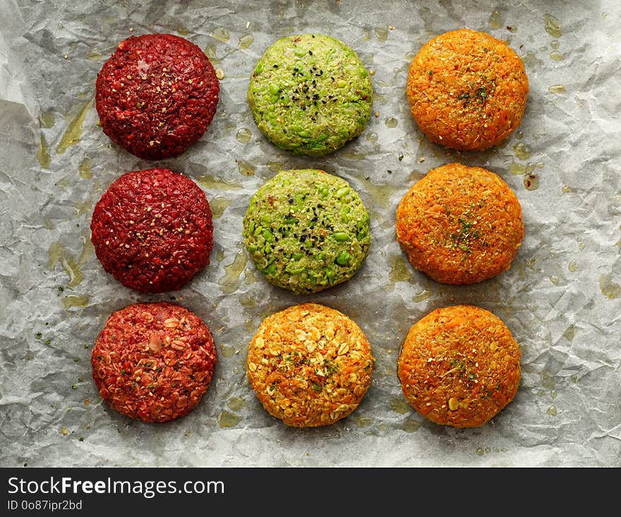 Raw vegan burgers made of beetroot, green peas, carrots, groats and herbs on white parchment prepared for baking, top view.